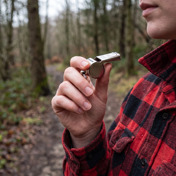 Loud Emergency Signal Whistle held up on a forest trail