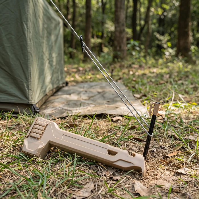 2-in-1 tent stake hammer with stake puller resting on grass beside a partly driven tent stake and guy line
